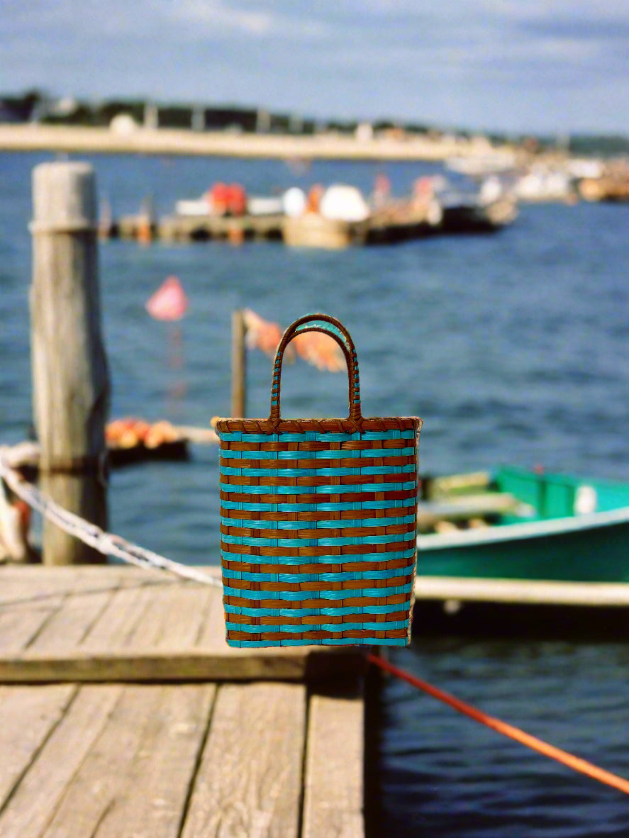 Woven bag with blue and brown pattern on a wooden dock by a body of water.