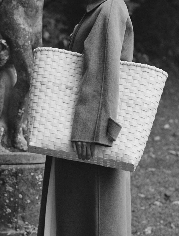 Woman holding a large woven basket in a park-like setting with a statue in the background