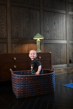 Child sitting in a woven basket in a room with wooden walls and a lamp.
