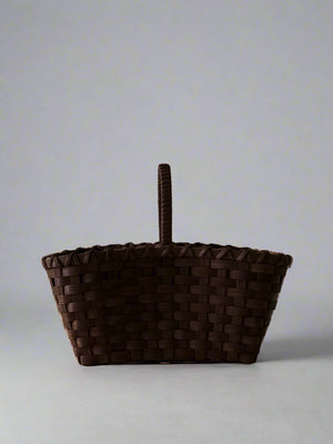 Woven brown basket with a handle on a light gray background
