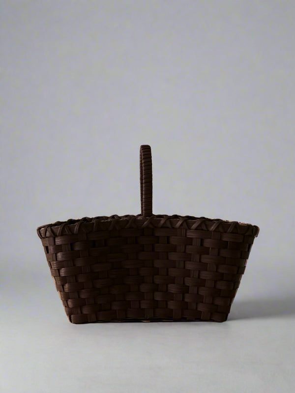 Woven brown basket with a handle on a light gray background