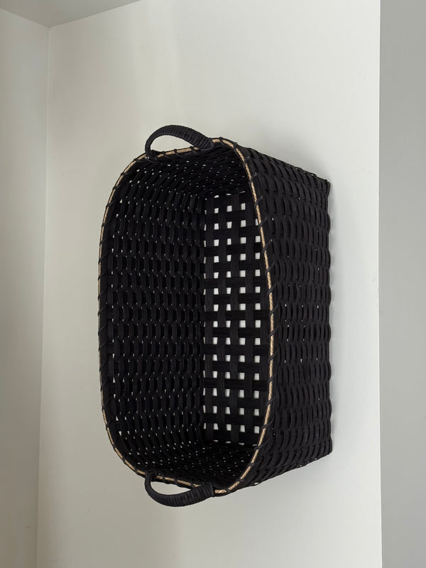 Black woven basket with a grid pattern on a white wall