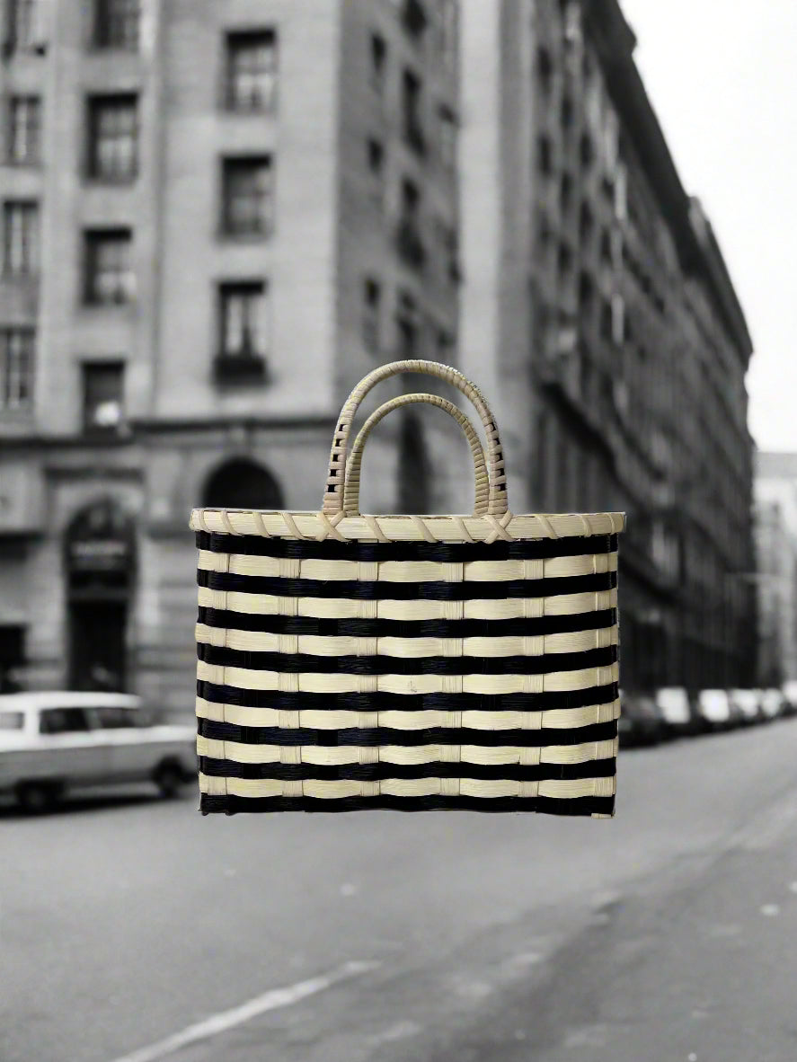 Black and white striped bag on a sandy beach with people and umbrellas in the background