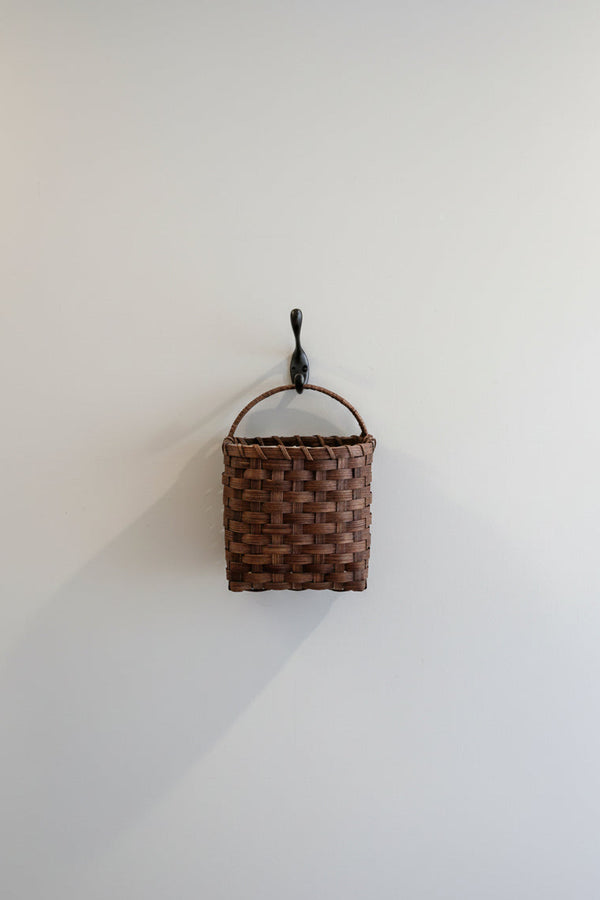 Brown woven wall basket with a black metal hook on a white wall