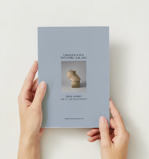 A person holding the packaging of a basket weaving kit with a image of a woven basket on the cover.